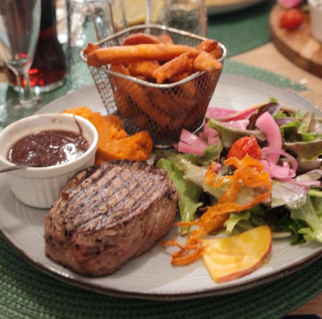 Un faux-filet grillé servi avec des frites de patate douce, une salade et une sauce