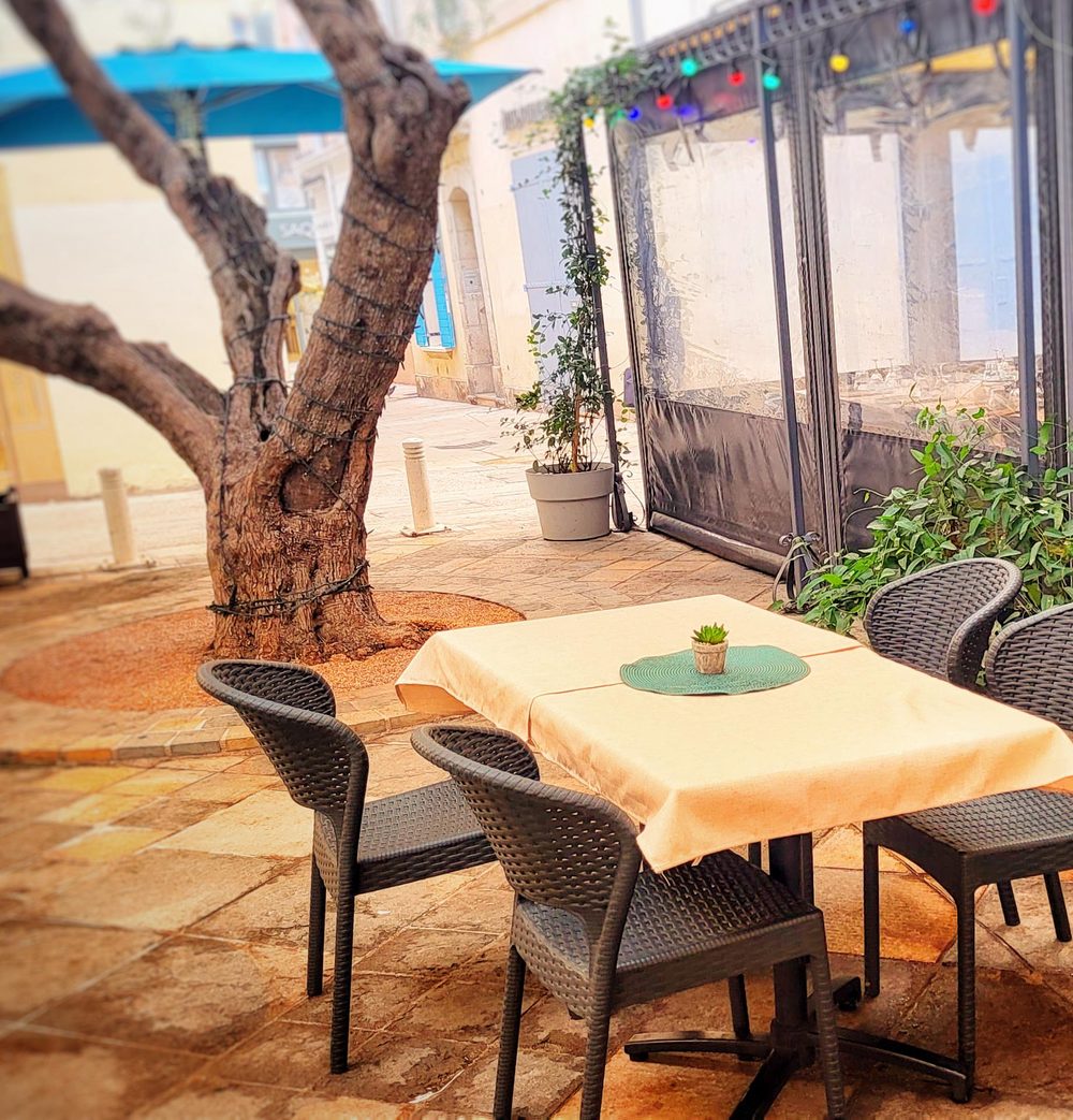 Une table nappée de jaune sous le vieil olivier de la place